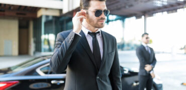 Handsome bodyguard listening to earpiece with car parked on street in city